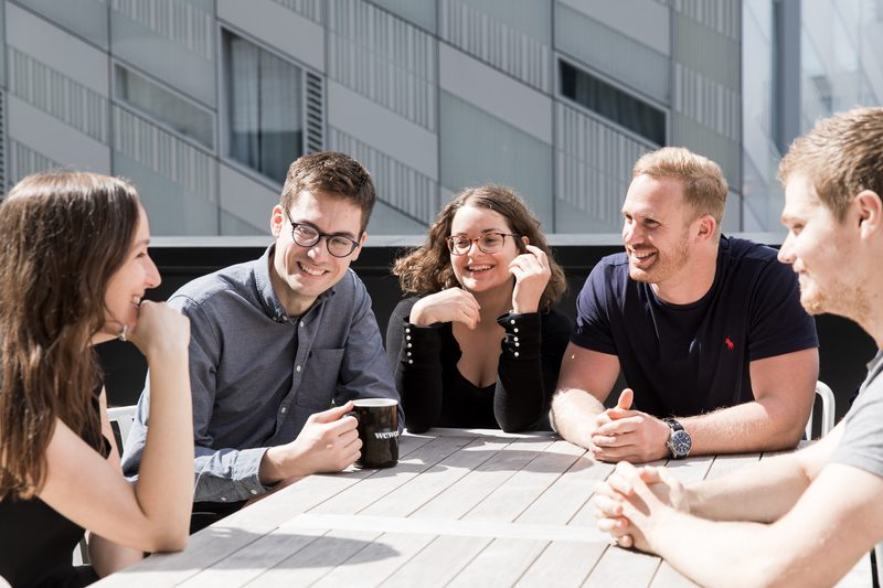 Five members of the Builtvisible team laughing together over coffee on the office terrace